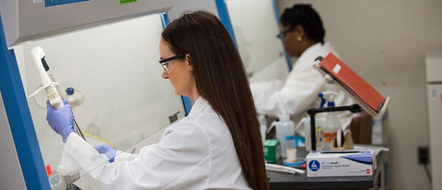 two women wearing white coats, using equipment in a lab